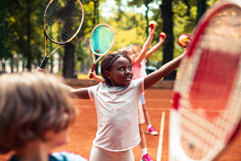 Children holding tennis balls and rackets.