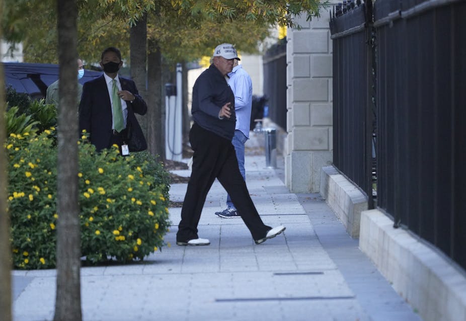 Donald Trump walking on pavement with security guard behind.