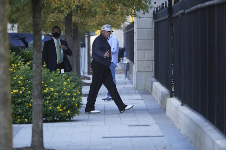 Donald Trump walking on pavement with security guard behind.