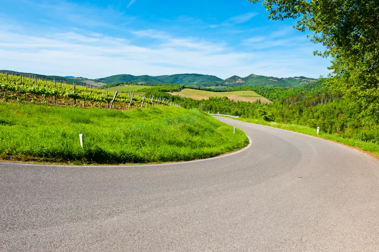 A bend in a paved road in the sunny Italian countryside.