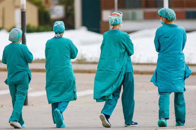 Cuatro sanitarios con su vestimenta de trabajo de espaldas caminando.