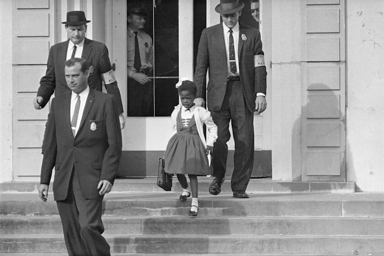 Men in suits escort a little girl in a dress outside of a building in an old photo..