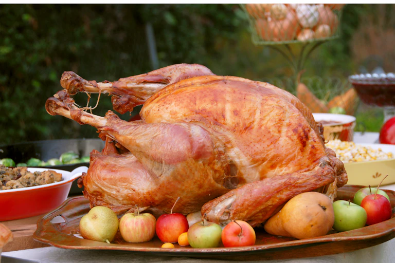 A cooked turkey sitting on a platter surrounded by apples on a table outside.