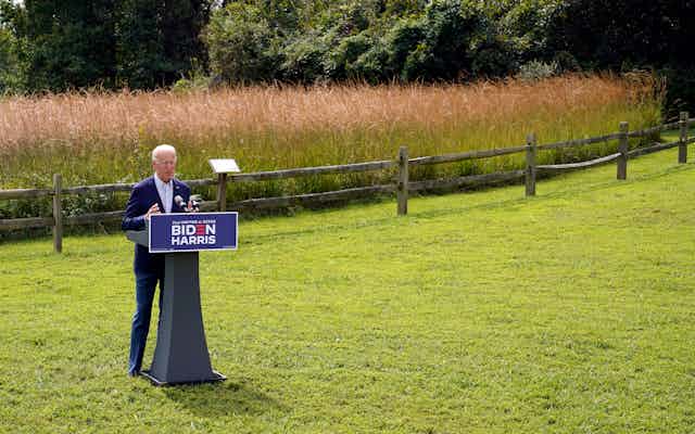 Biden stands in front of a podium with a wheat field behind him.