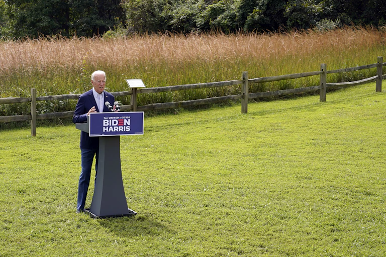 Biden stands in front of a podium with a wheat field behind him.