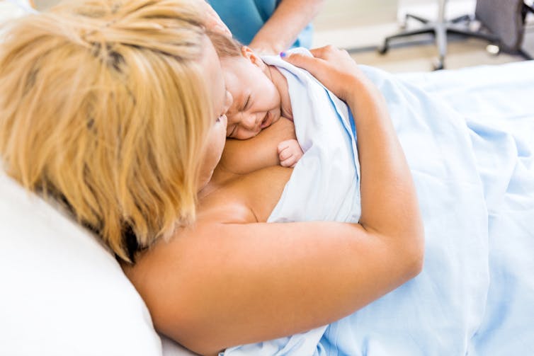 A mother with her infant on her chest, covered by a sheet.