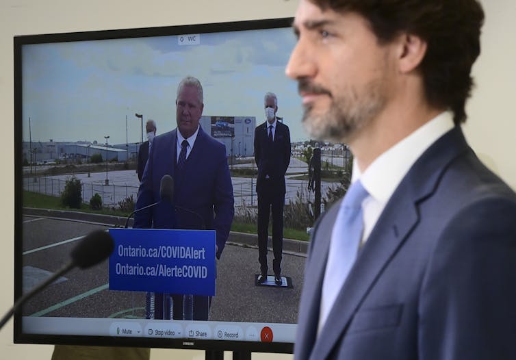 Justin Trudeau speaks at a news conference while Doug Ford appears on a screen beside him.