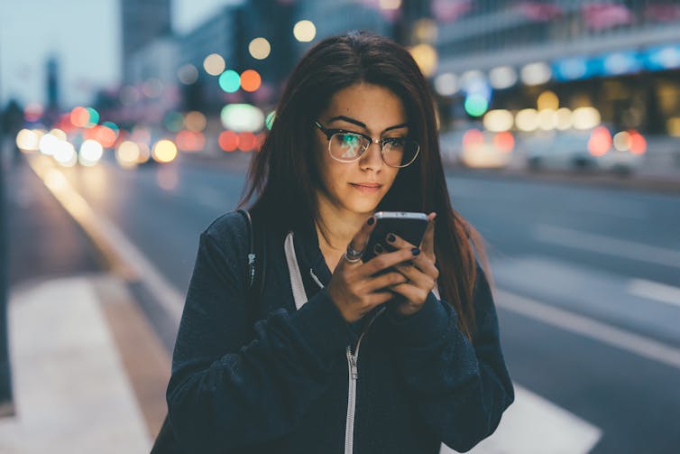 A woman looks at her phone in the twilight.