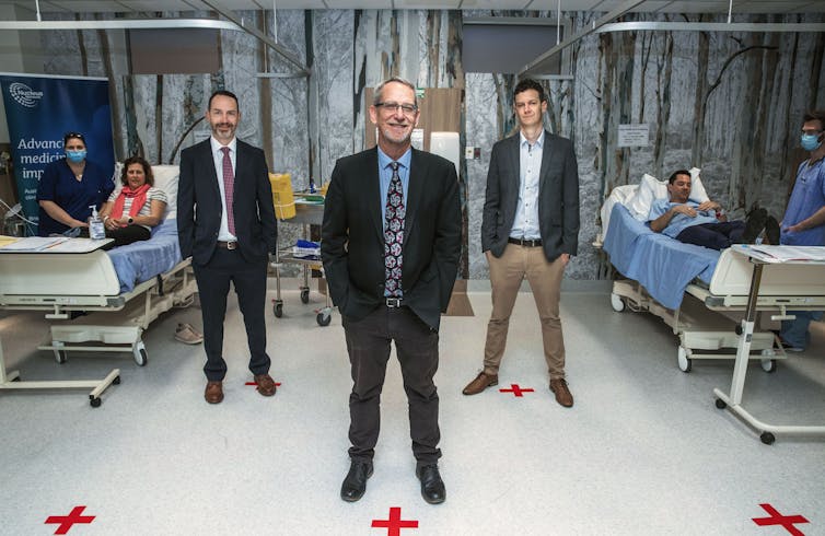 Researchers standing in a room with patients and nurses.