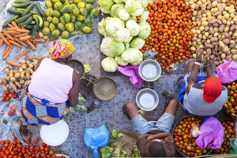 Two women and a child selling a selection of fresh vegetables on a street market.