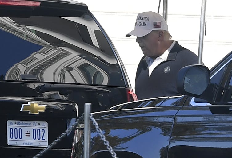 Donald Trump wearing a MAGA hat and dressed in golfing attire getting into a car.