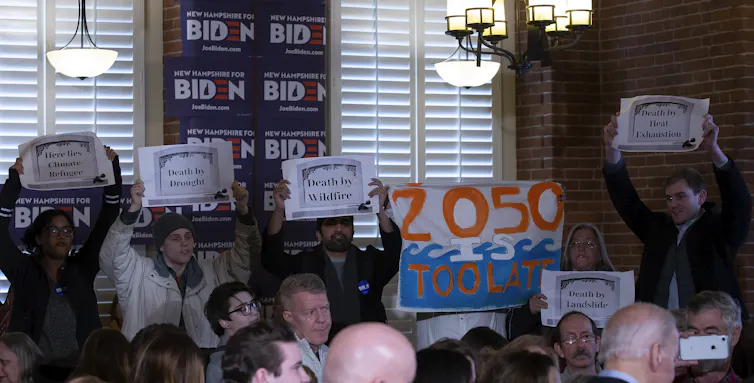 Protesters hold signs warning about climate change at a Democratic Primary event for Joe Biden's campaign.
