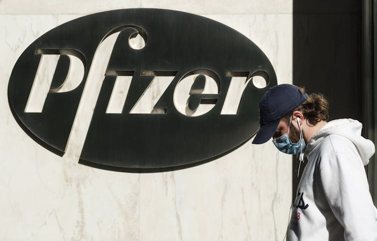 Man wearing a face mask walks past Pfizer sign on building.