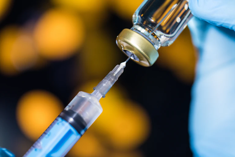 Hypodermic needle piercing a vaccine vial.