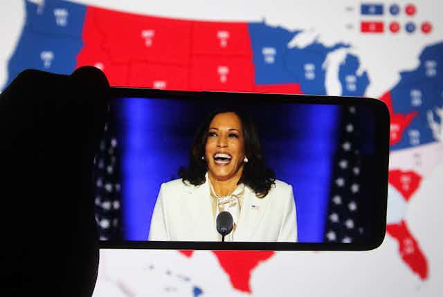Kamala Harris vue sur un smartphone, sur fond de carte électorale des États-Unis