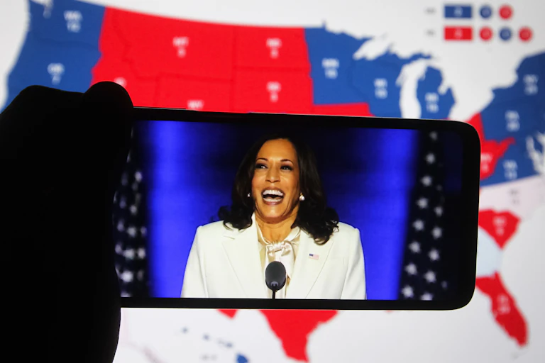 Kamala Harris vue sur un smartphone, sur fond de carte électorale des États-Unis