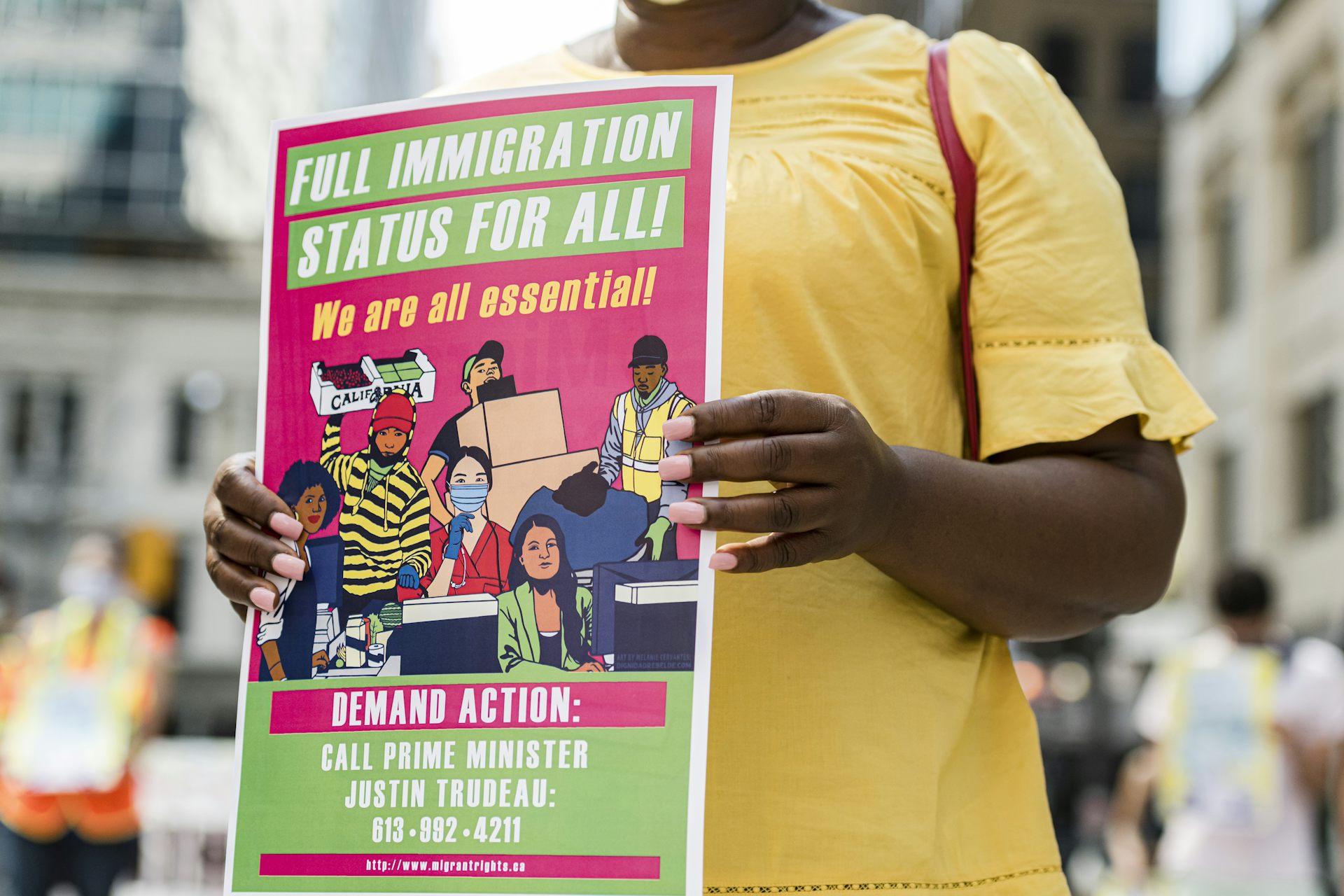 A woman carries a sign during a protest for migrant worker rights. The sign reads: full immigration status for all.