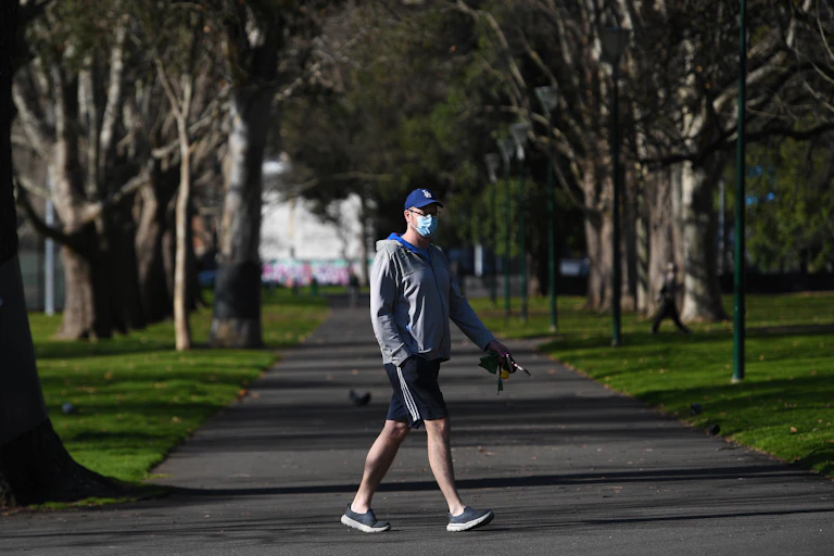 A mean wearing a mask walks through a park.