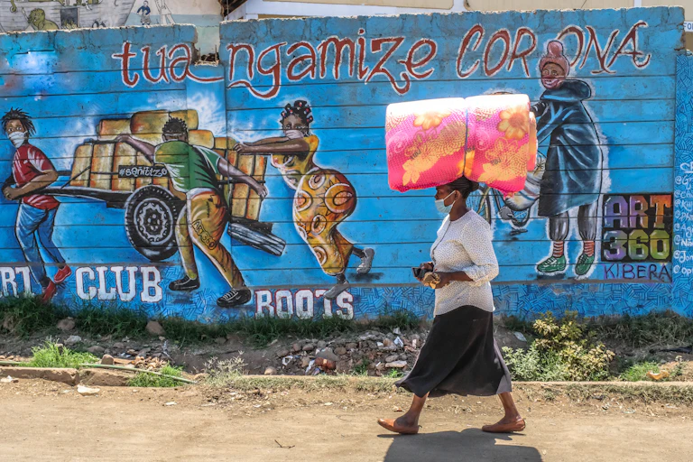 A woman wearing a facemask is seen carrying luggage as she walks past a wall with Covid-19 artistic information