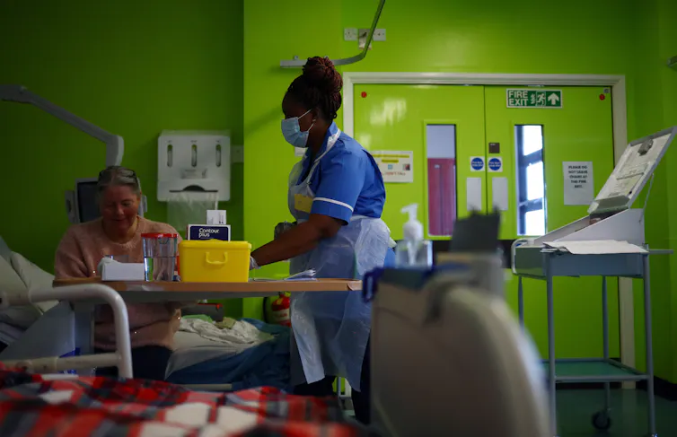 A black British nurse working in a ward, wearing PPE