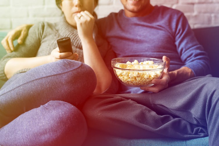 Man and woman watching TV together on sofa with popcorn.