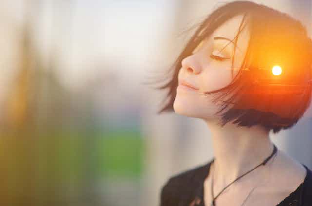 Mujer con el rostro feliz y ojos cerrados y una puesta de sol reflejada en el lateral de su cabeza.