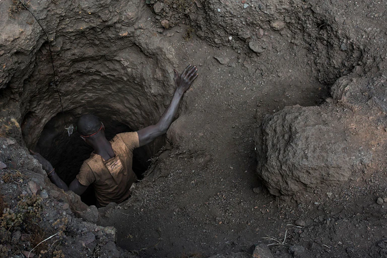 A man, seen from above, getting into a hole in the ground