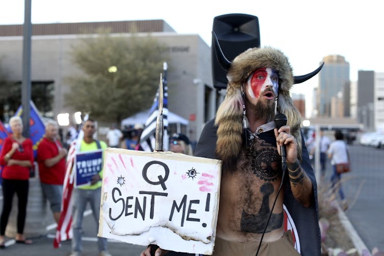 A Qanon believer speaking to a public crowd.