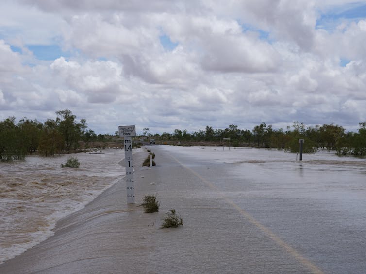 A flooded road in the Northern Territory with a flood marker.