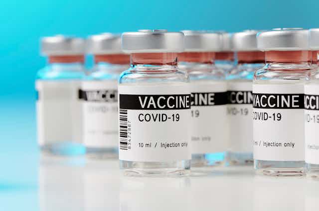 Bottles of COVID-19 vaccine on white countertop against blue background 