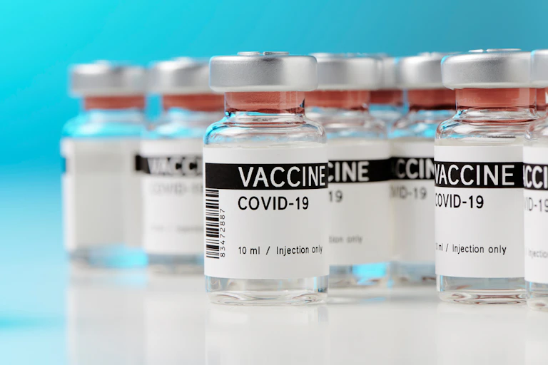 Bottles of COVID-19 vaccine on white countertop against blue background