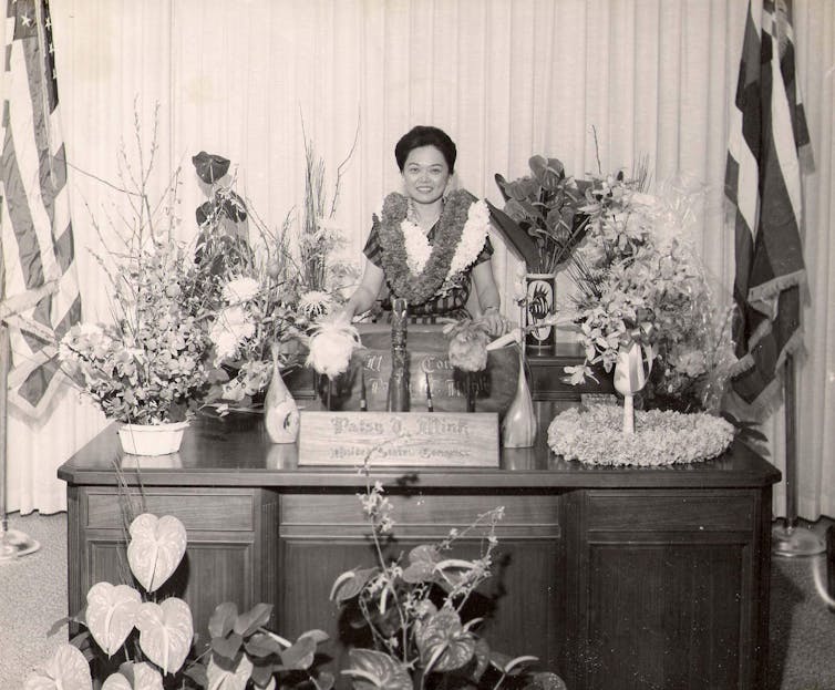 Black and white image of Mink wearing a lei and surrounded by flowers