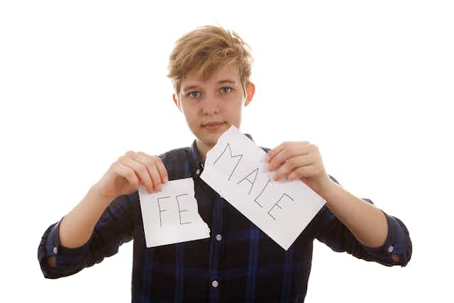 Young trans person tears up paper into two pieces bearing letters 'FE' and 'MALE',