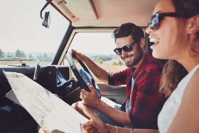 Young couple on a roadtrip, man driving, woman map reading
