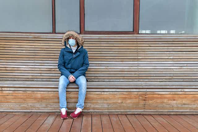 Una persona con mascarilla y abrigo sentada en un banco,