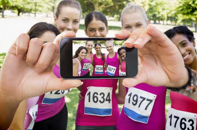 Mujeres con ropa deportiva rosa participantes en una carrera contra el cancer de mama se hacen una fotografía con un móvil.