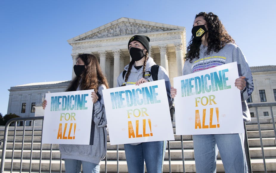 Protesters with signs stand in front of the U.S. Supreme Court building.