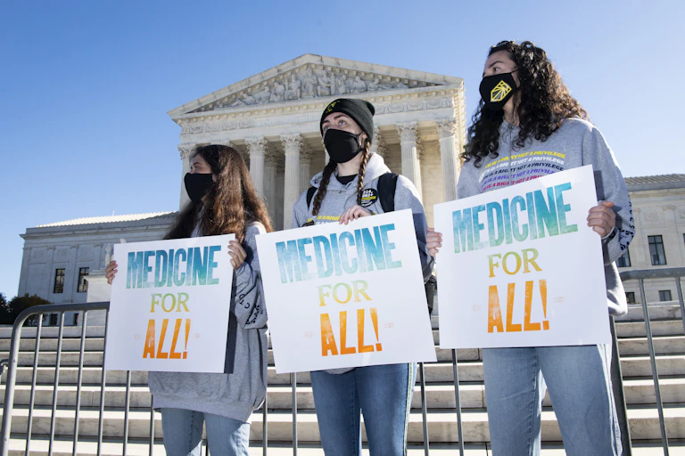 Protesters with signs stand in front of the U.S. Supreme Court building.