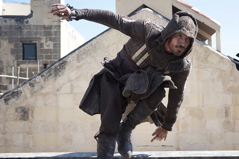 Michael Fassbender jumping over a wall dressed as a medieval assasin.