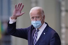 Biden, wearing a mask, waves to photographers.