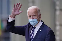 Biden, wearing a mask, waves to photographers.