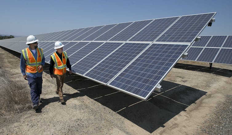 Two people walking in front of a large solar panel at a solar farm.