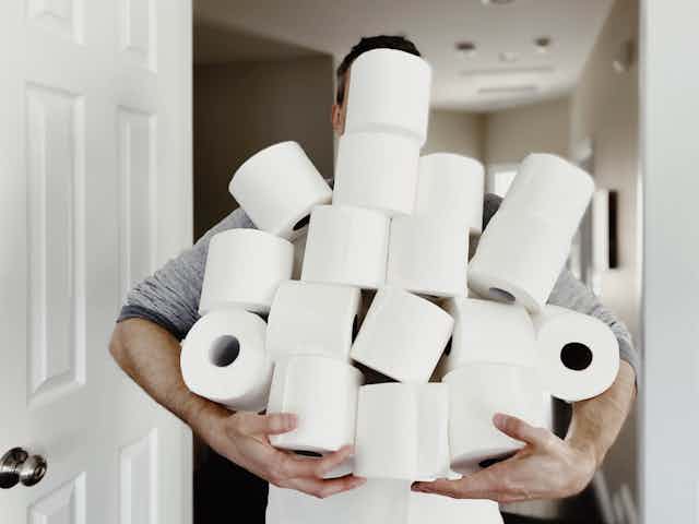 A man carries an armful of toilet paper.