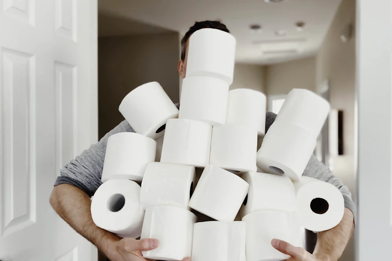 A man carries an armful of toilet paper.