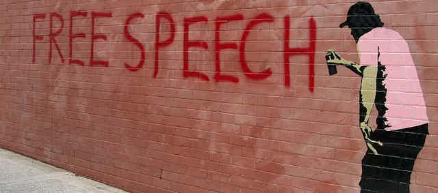 A mural of a man painting the words free speech on a wall