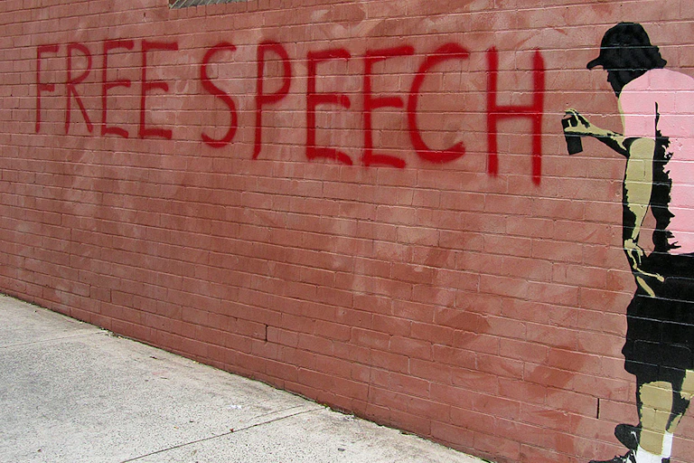 A mural of a man painting the words free speech on a wall