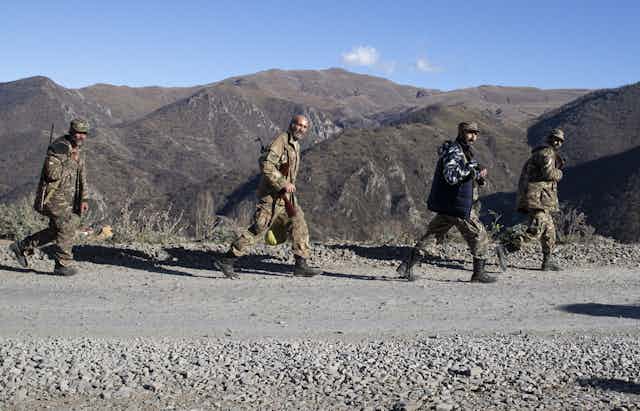Servicemen in fatigues walk along a gravel road with tower mountains in the background