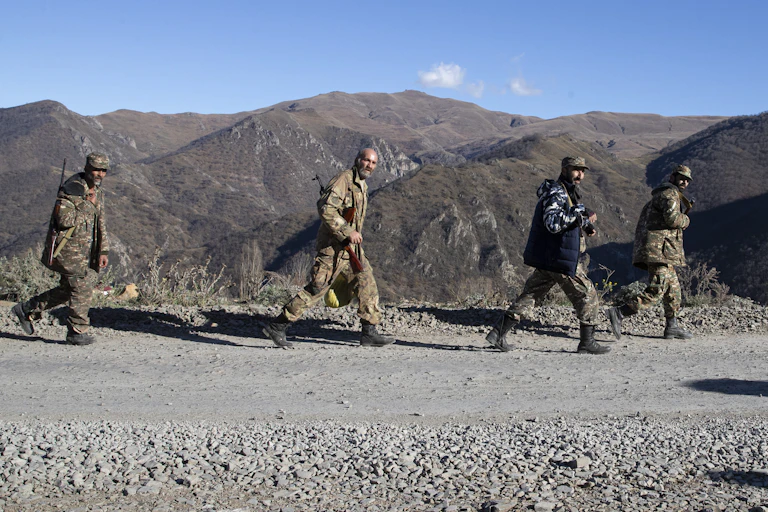 Servicemen in fatigues walk along a gravel road with tower mountains in the background