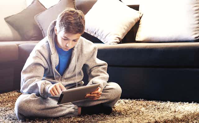 Teenage boy sitting on the floor, looking at his iPad.