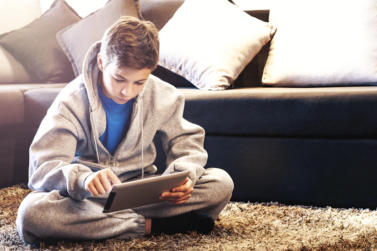 Teenage boy sitting on the floor, looking at his iPad.